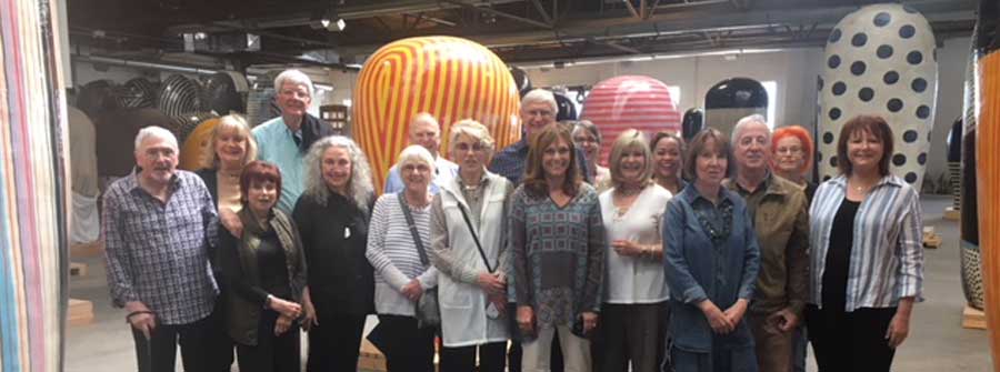9 of 10, Large group of people posing in an artist studio with colorful sculptures in the background